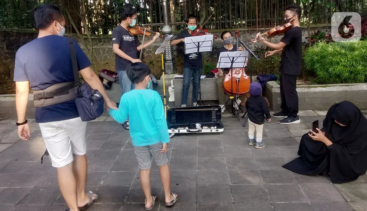 Warga menyaksikan penampilan musisi lokal Bogor yang tengah memainkan musik klasik di pedestrian Kebun Raya, Jalan Pajajaran, Bogor, Jawa Barat, Minggu (14/6/2020). Mereka mengamen untuk memenuhi kebutuhan hidup akibat sepinya job pertunjukan selama pandemi COVID-19. (merdeka.com/Arie Basuki)