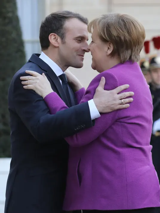 Presiden Prancis Emmanuel Macron (kiri) berpelukan dengan Kanselir Jerman Angela Merkel saat menyambut kedatangannya di Istana Presiden Eylsee di Paris (16/3). (AFP Photo/Ludovic Marin)