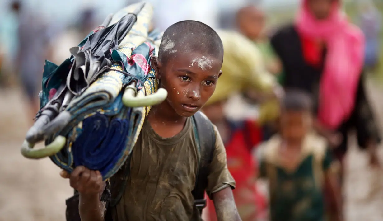 Seorang anak etnis Rohingya dari Myanmar memanggul tikar ketika melewati sawah untuk menyebrang ke perbatasan Bangladesh, wilayah Teknaf yang berada di distrik Cox's Bazar, 1 September 2017. (AP Photo/Bernat Armangue)