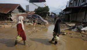 Hingga Kamis (5/12/2025) malam, listrik belum menyala, sehingga jalanan masih gelap gulita. Tampak dalam foto, para penyintas berjalan melewati reruntuhan mobil di area terdampak banjir bandang di Aceh Tamiang, Sumatera, Indonesia, Kamis 4 Desember 2025. (AP Photo/Binsar Bakkara)