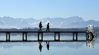 Pejalan kaki berjalan melewati panorama pegunungan alpine di danau Starnberger See, Jerman (25/2). Pegunungan ini membentang dari Austria dan Slovenia di timur, melalui Italia, Swiss, Liechtenstein, Jerman sampai ke Prancis. (AFP Photo/Christof Stache)