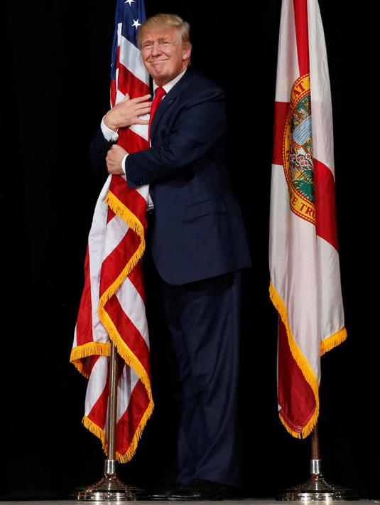 Donald Trump memeluk bendera AS saat kampanye di Tampa, Florida, AS (24/10). Sekitar 2.000 pendukung Donald Trump di Florida menyaksikan Capres AS tersebut berkampanye. (REUTERS/Jonathan Ernst)