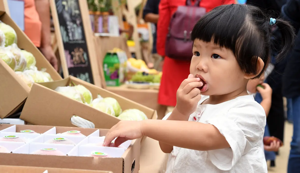 Seorang gadis kecil mencicipi produk-produk pertanian pada acara perayaan untuk menandai festival panen petani China di Distrik Pinggu, Beijing, ibu kota China, pada 24 September 2020. (Xinhua/Ren Chao)