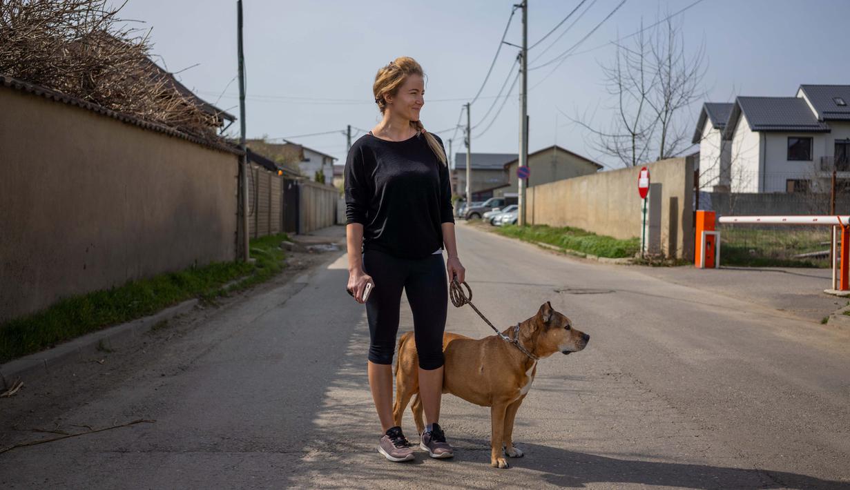 Silvia Rad (34) berpose dengan anjingnya Sa'id (12) saat perjalanan di Bucharest (28/3/2020). Undang-undang militer, yang disahkan pemerintah Rumania untuk mengurangi penyebaran virus corona, menyatakan berjalan bersama anjing adalah salah satu  kegiatan yang masih diizinkan. (AFP/Andrei Pungovschi)