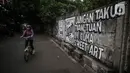 Pengendara sepeda melintas di depan mural di kawasan Jakarta Pusat. Selasa (24/8/2021). Banyak beberapa tempat mural yang menyuarakan kebebasan berpendapat saat ini menjadi viral lantaran dihapus oleh petugas. (Liputan6.com/Johan Tallo)