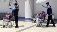 Petugas haji memayungi jemaah haji lansia yang baru tiba di Bandara Prince Mohammed bin Abdulaziz Madinah via jalur fast track. (dok. Dinny Mutiah/MCH 2025)
