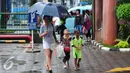 Dua pengojek payung cilik mengikuti  wanita yang memakai jasa ojek payung mereka di Jakarta, Selasa (1/11). Musim hujan membawa berkah bagi anak-anak tersebut karena bisa mendapatkan rezeki lebih dari jasa ojek payung. (Liputan6.com/Angga Yuniar)