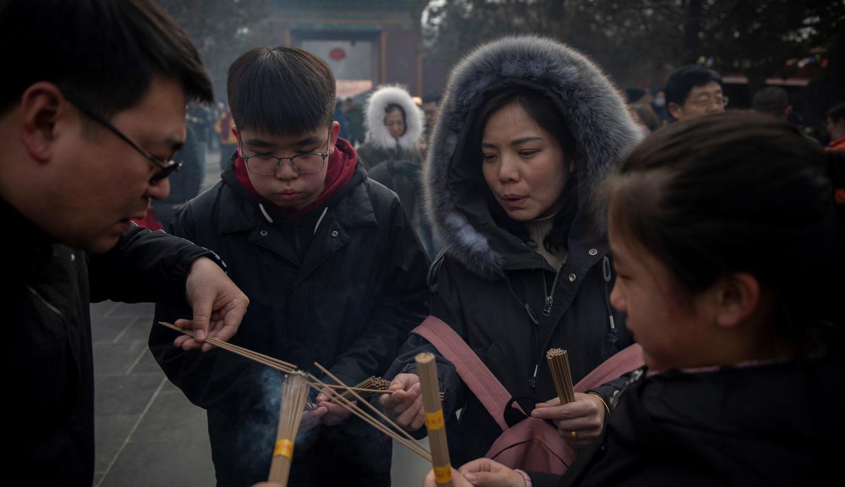 Keluarga membakar dupa untuk berdoa keberuntungan pada hari kelima Tahun Baru Imlek di Yonghegong, atau Kuil Lama di Beijing (9/2). Warga China merayakan Tahun Babi tersebut dengan doa, pesta keluarga, dan belanja. (AFP Photo/Nicolas Asfouri)