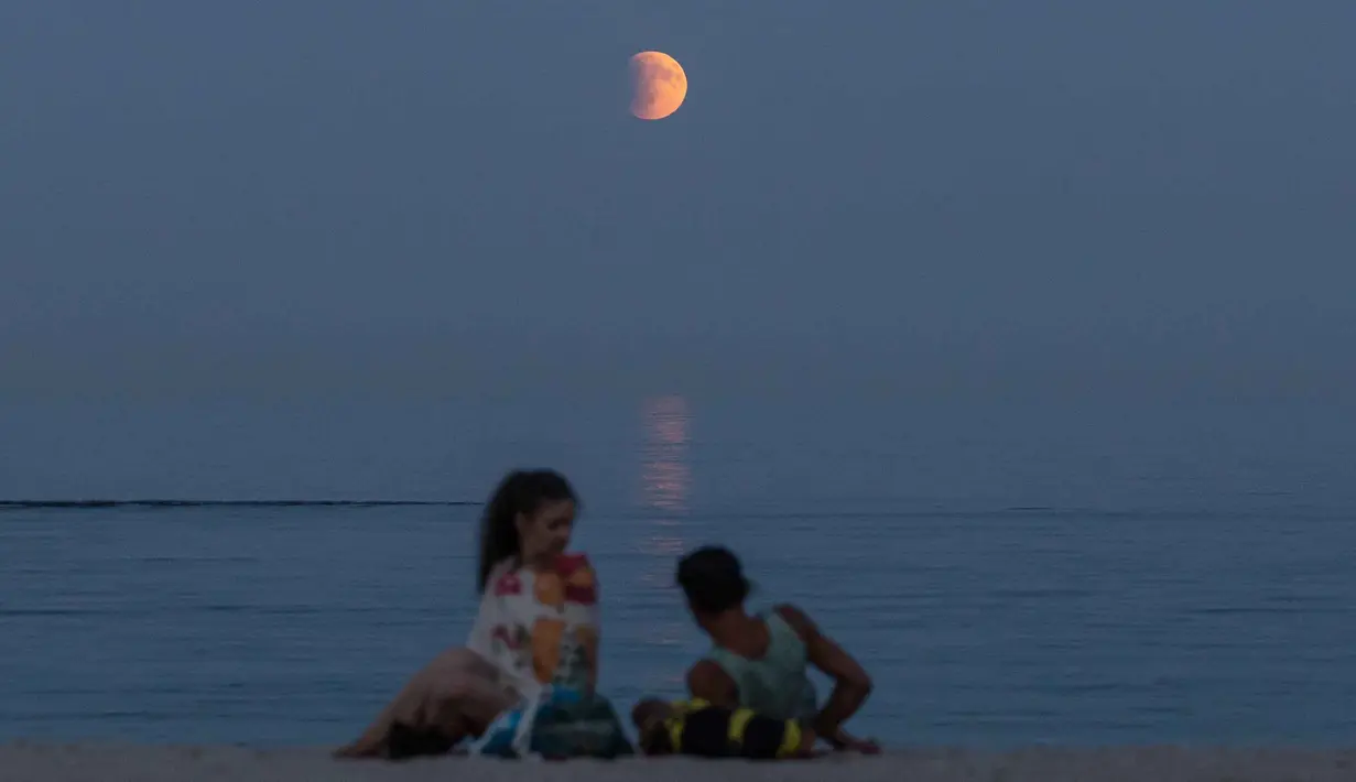 Fenomena ini merupakan gerhana bulan total kedua yang berlangsung sepanjang tahun 2025. Tampak dalam foto, para pengunjung pantai beristirahat di tepi pantai Laut Hitam dengan bulan purnama yang juga dikenal sebagai “Blood Moon” selama fase gerhana bulan total di latar belakang di Odesa, Ukraina pada 7 September 2025. (Oleksandr GIMANOV/AFP)