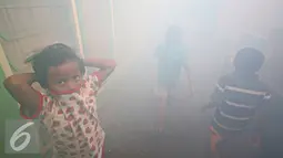 Sejumlah anak berada saat fogging di kawasan padat penduduk di Kebon Nanas, Jakarta, Jumat (15/4). Fogging tersebut dilakukan untuk mencegah berkembangbiaknya nyamuk aedes aegypti penyebab penyakit demam berdarah dengue. (Liputan6.com/Immanuel Antonius)