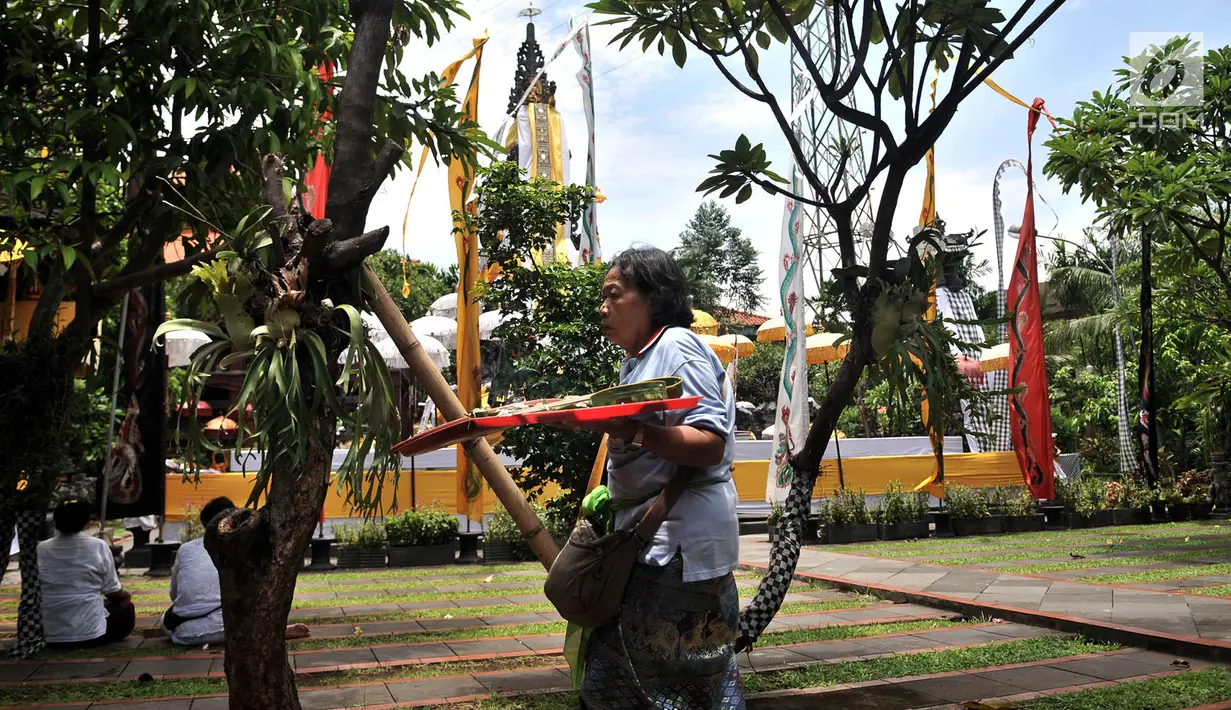 Umat Hindu membawa sajen melintasi Pura Utama di Pura Aditya Jaya, Jakarta, Senin (4/3). Ngayah merupakan tradisi yang dilakukan gotong-royong oleh kaum perempuan Hindu dalam membuat sajen untuk persiapan sembahyang  Nyepi. (merdeka.com/Iqbal S. Nugroho)
