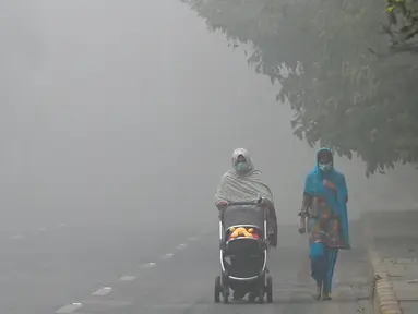 Seorang wanita berjalan di sepanjang jalan yang diselimuti kabut asap di Lahore pada Kamis 14 November 2024. (Arif ALI/AFP)