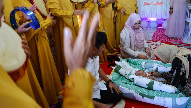 Seorang bayi menjalani ritual 'peutron tanoh aneuk' (turun tanah anak) di Banda Aceh, Aceh, Senin (15/7/2019). Ritual turun tanah anak telah menjadi tradisi sakral bagi masyarakat Aceh yang dilaksanakan pada saat bayi berusia 44 hari. (CHAIDEER MAHYUDDIN / AFP)