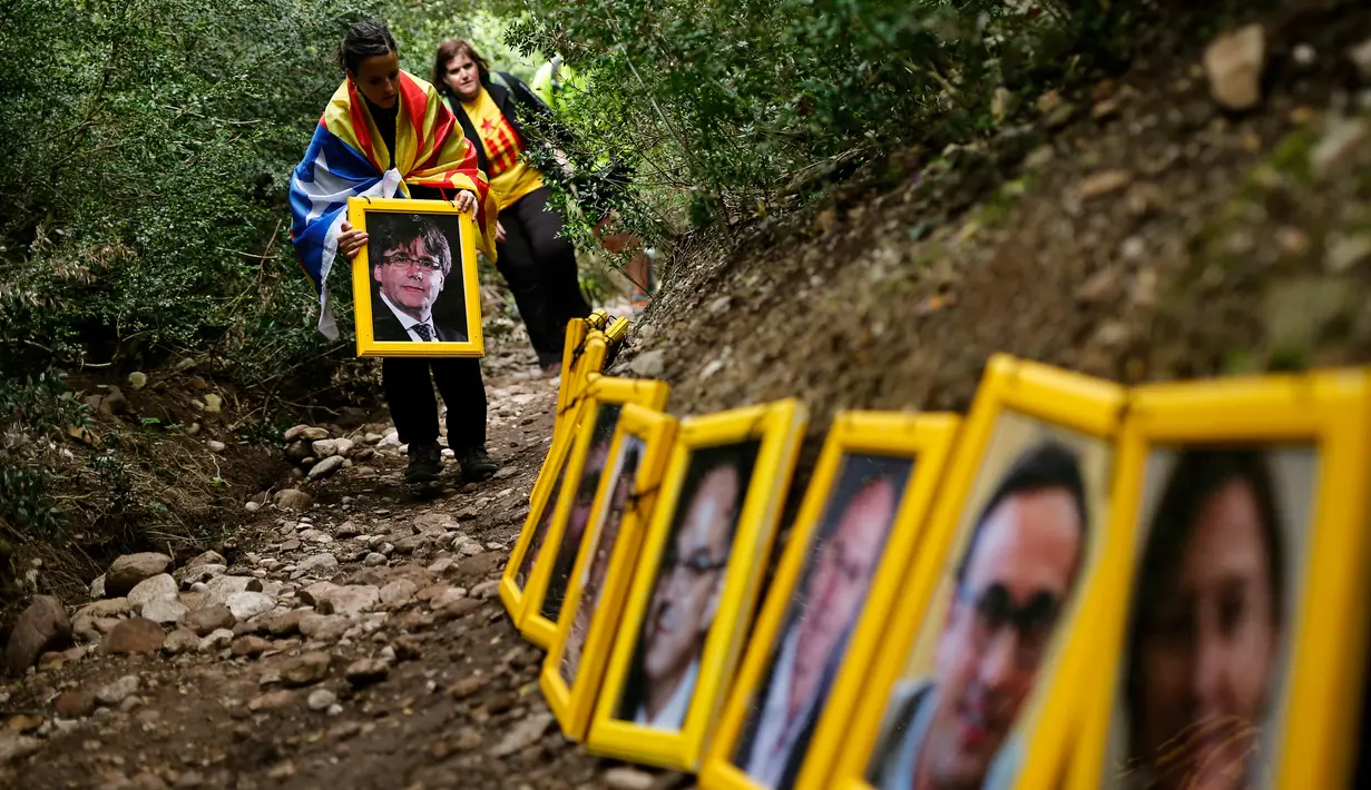 Seorang wanita memegang foto presiden terguling Catalonia, Carles Puigdemont saat mereka menjejerkan potret orang-orang yang dipenjara dan diasingkan di Gunung Montserrat, Spanyol (28/4). (AFP/Pau Barrena)