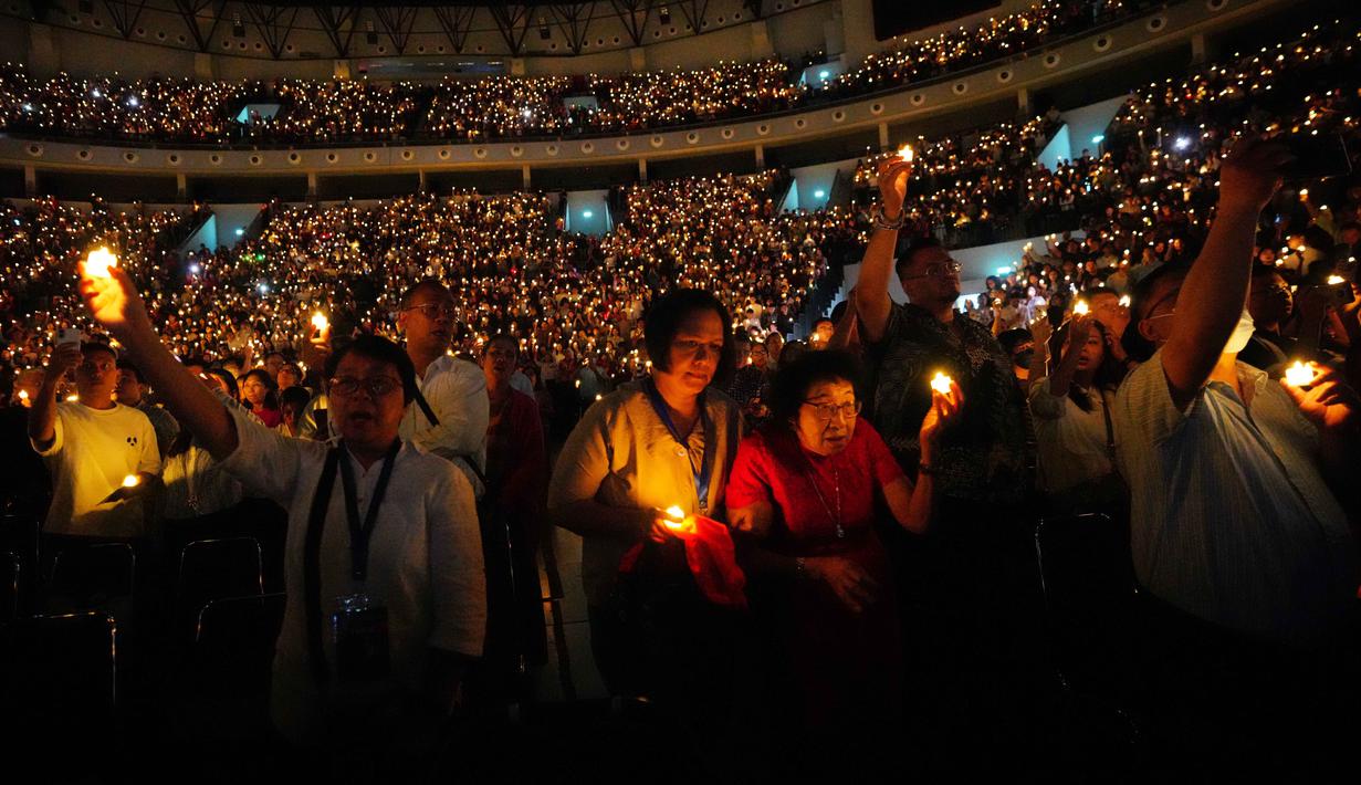 Sekitar 16.000 jemaat dari wilayah Jabodetabek memadati arena untuk mengikuti ibadah tersebut. Tampak dalam foto, orang-orang memegang lilin elektrik sambil bernyanyi selama kebaktian Malam Natal di Indonesia Arena, Kompleks Gelora Bung Karno, Jakarta, Rabu 24 Desember 2025. (AP Photo/Tatan Syuflana)