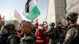 Pengunjuk rasa berkostum sinterklas (Santa Claus) berhadapan dengan polisi perbatasan Israel dalam demonstrasi di Bethlehem, Tepi Barat, 23 Desember 2017. Protes terkait pengakuan Donald Trump atas Yerusalem sebagai Ibu Kota Israel. (AP/Nasser Shiyoukhi)