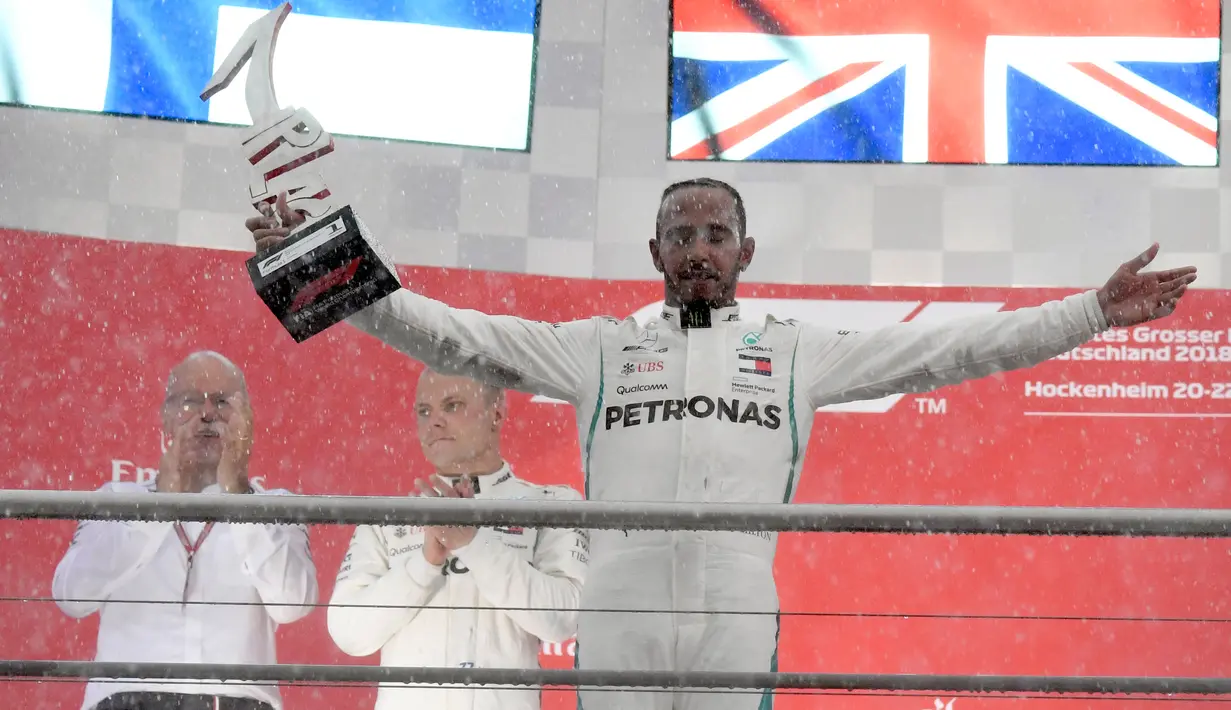 Pembalap Mercedes, Lewis Hamilton memegang trofi juara F1 GP Jerman di atas podium  Sirkuit Hockenheim, Minggu (22/7). Kemenangan ini diraih secara dramatis karena Hamilton mengawali balapan dari urutan ke-14. (AP/Jens Meyer)