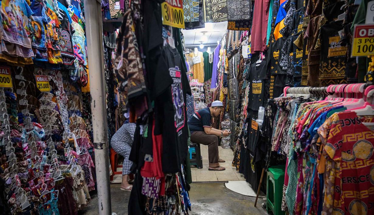 Kawasan ini menjadi tujuan utama warga Surabaya dan sekitarnya untuk berburu takjil dengan harga terjangkau maupun berziarah ke makam Sunan Ampel. Tampak dalam foto, seorang penjual pakaian menggunakan telepon seluler sambil menunggu pelanggan selama bulan suci Ramadan di dekat Masjid Sunan Ampel, Surabaya, Jawa Timur, pada Minggu 8 Maret 2026. (JUNI KRISWANTO/AFP)
