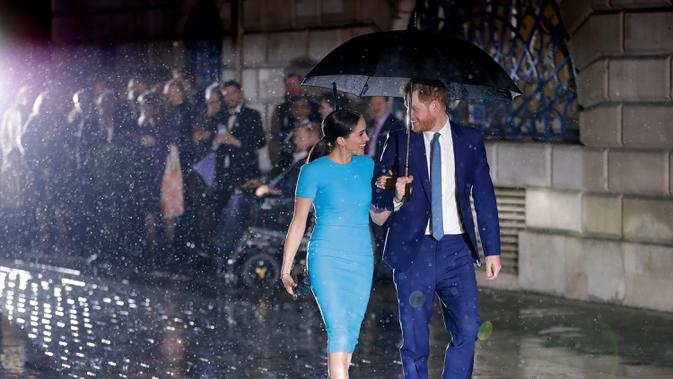 Pangeran Harry dan Meghan Markle sepayung berdua saat tiba di Endeavour Fund Awards, London, Inggris, Kamis (5/3/2020). Hujan lebat turun saat Pangeran Harry dan Meghan Markle tiba di lokasi. (AP Photo/Kirsty Wigglesworth)