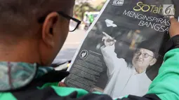 Warga membaca koran sambil menunggu di sisi jalan TMP Kalibata untuk melihat prosesi pemakaman Presiden RI ke-3 BJ Habibie, Jakarta, Kamis (12/9/2019). BJ Habibie meninggal pada Rabu (11/9/2019) pukul 18.05 WIB di usia 83 tahun. (Liputan6.com/Helmi Fithriansyah)