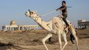 Seorang joki Palestina beraksi saat bersaing dalam perlombaan unta lokal yang diadakan di lokasi bekas bandara Gaza yang hancur, di Rafah, Jalur Gaza selatan (20/10/2019). Bandara Internasional Yasser Arafat yang diresmikan November 1998, kini tinggal reruntuhan akibat serangan Israel. (AFP Photo/Sa
