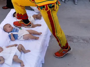 Pria berkostum setan melompati bayi-bayi yang terlentang di atas matras di sebuah jalan selama festival El Colacho di desa Castrillo de Murcia, Spanyol, Minggu (18/6). Festival melompati bayi ini sudah menjadi perayaan tahunan sejak 1620 (CESAR MANSO/AFP)