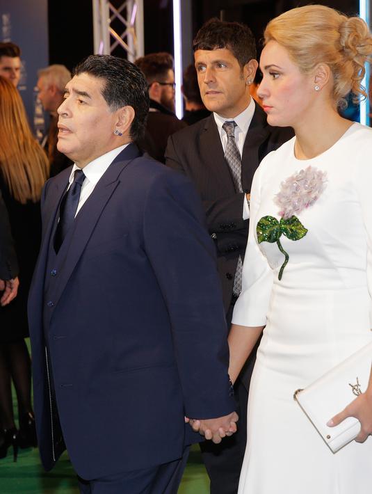 Pesepakbola legendaris Argentina, Diego Maradona mengandeng tangan kekasihnya, Rocio Oliva saat tiba menghadiri The Best FIFA Football Awards 2017 di London, (23/10). Rocio Oliva merupakan mantan pemain sepak bola wanita. (AP Photo/Alastair Grant)