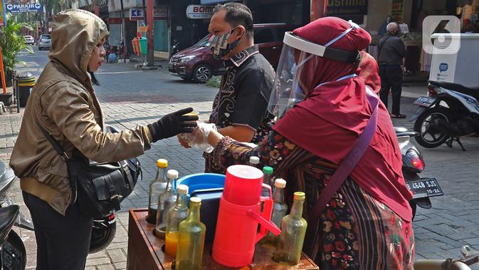Tidar (46), melayani pembeli di Pasar Baru, Jakarta, Kamis (11/06/2020). Penjual jamu tradisional keliling ini tampak mematuhi protokol kesehatan pencegahan COVID-19 dengan mengenakan masker, face shield, dan sarung tangan dalam melayani pelanggan setianya. (Liputan6.com/Herman Zakharia)