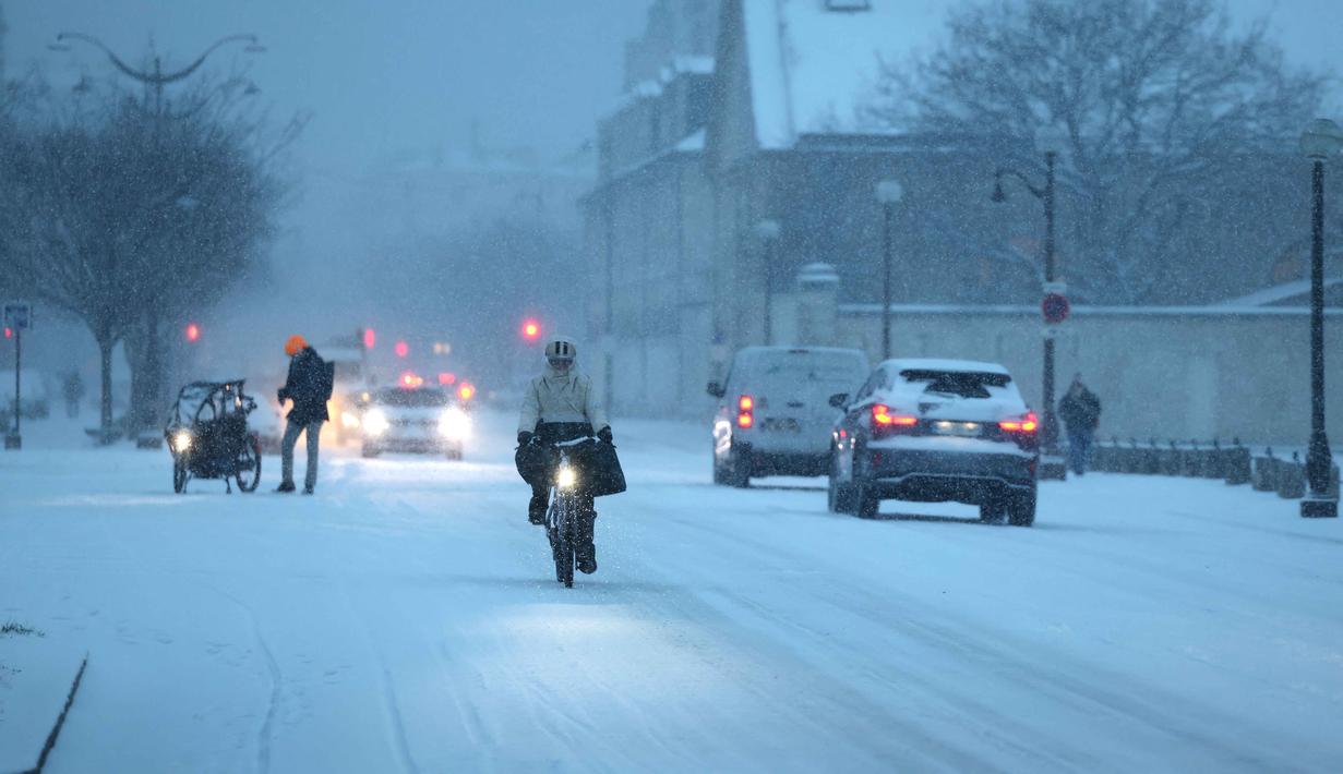 Menteri Transportasi Prancis, Philippe Tabarot, memperingatkan hujan salju diperkirakan masih akan berlanjut dan telah menetapkan status waspada oranye di 38 distrik. Tampak dalam foto, mobil, pejalan kaki, dan pesepeda tetap beraktivitas meskipun bersalju di Paris pada 7 Januari 2026. (Ludovic MARIN/AFP)