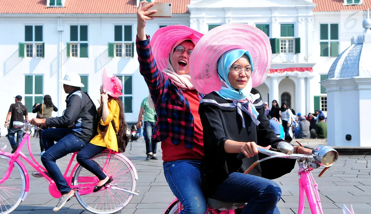 Pengunjung berswafoto sambil menaiki sepeda Onthel di Kawasan Kota Tua, Jakarta, Kamis (21/9). Kawasan Kota Tua menjadi salah satu tujuan warga Jakarta dan sekitarnya untuk mengisi libur Tahun Baru Islam. (Liputan6.com/Helmi Afandi)