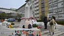 Orang-orang berdiri di depan patung Yohanes Paulus II di luar Rumah Sakit Universitas Gemelli tempat Paus Fransiskus dirawat karena pneumonia, di Roma pada 8 Maret 2025. (ANDREAS SOLARO/AFP atau pemberi lisensi/AFP)