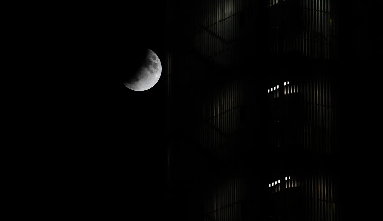 Fenomena gerhana bulan sebagian (parsial) terlihat di atas gedung pencakar langit di distrik EUR Roma di Italia pada Selasa (16/7/2019). Gerhana bulan parsial ini bisa diamati dari Amerika Selatan, Eropa, Afrika, Asia dan Australia. (Andreas SOLARO/AFP)