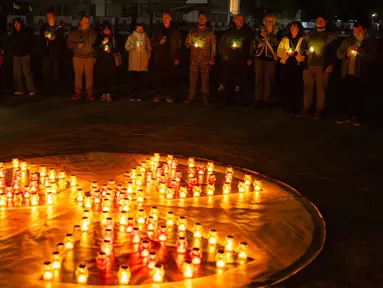 Orang-orang memegang lilin di depan simbol bahaya radiasi di sebuah monumen yang didedikasikan untuk petugas pemadam kebakaran dan pekerja yang meninggal setelah bencana nuklir Chernobyl, menjelang peringatan 40 tahunnya di Slavutych, Ukraina, Sabtu, 25 April 2026. (AP Photo/Dan Bashakov)
