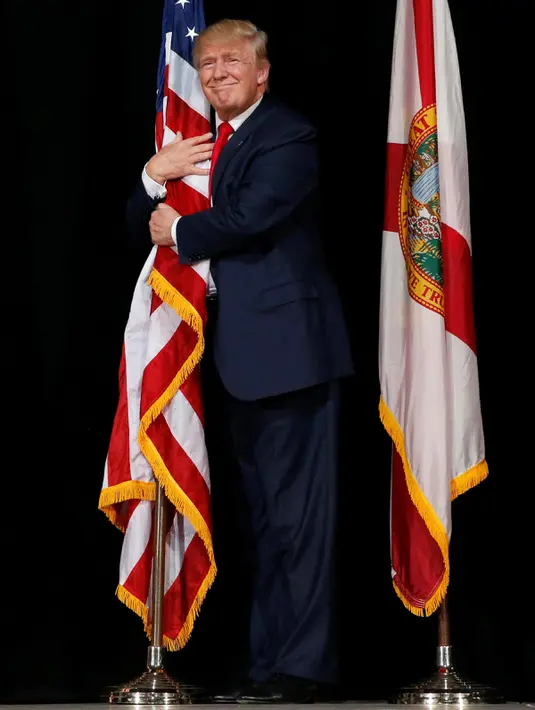 Donald Trump memeluk bendera AS saat kampanye di Tampa, Florida, AS (24/10). Sekitar 2.000 pendukung Donald Trump di Florida menyaksikan Capres AS tersebut berkampanye. (REUTERS/Jonathan Ernst)