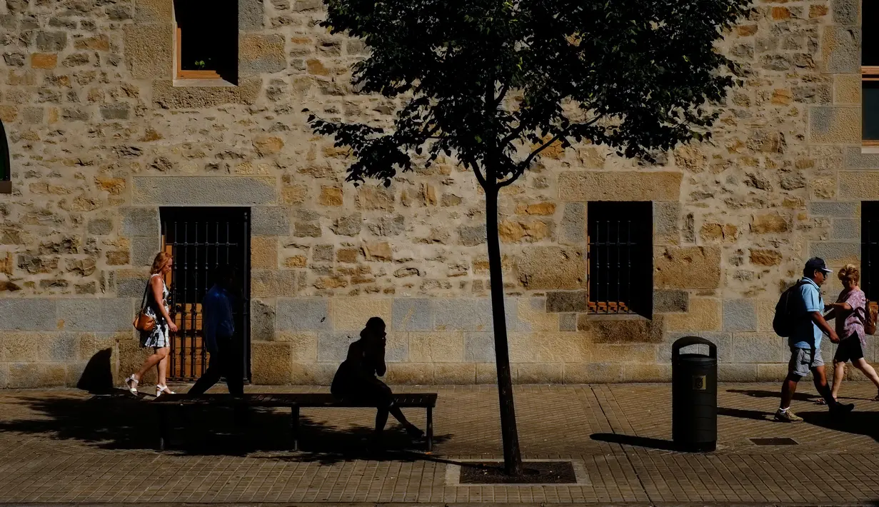 Seorang wanita berteduh di bawah pohon sambil menunggu bus saat musim panas, di Pamplona, Spanyol utara, (3/8). Dua orang tewas akibat sengatan panas di Spanyol ketika Eropa dilanda gelombang panas. (AP Photo/Alvaro Barrientos)