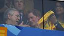 Dari balik kaca pelindung, Pangeran Harry terlihat memamerkan kaos Timnas Brasil kepada salah satu penonton yang ikut menyaksikan laga Brasil vs Kamerun di Stadion Nasional Brasil, (24/6/2014). (REUTERS/Ueslei Marcelino)
