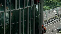 Pekerja saat membersihkan kaca gedung bertingkat di kawasan Kuningan, Jakarta, Minggu (19/12/2021). Pekerja ini harus bergelantungan dengan seutas tali untuk membersihkan dinding-dinding gedung bertingkat yang tingginya kurang lebih mencapai 150 meter. (Liputan6.com/Johan Tallo)