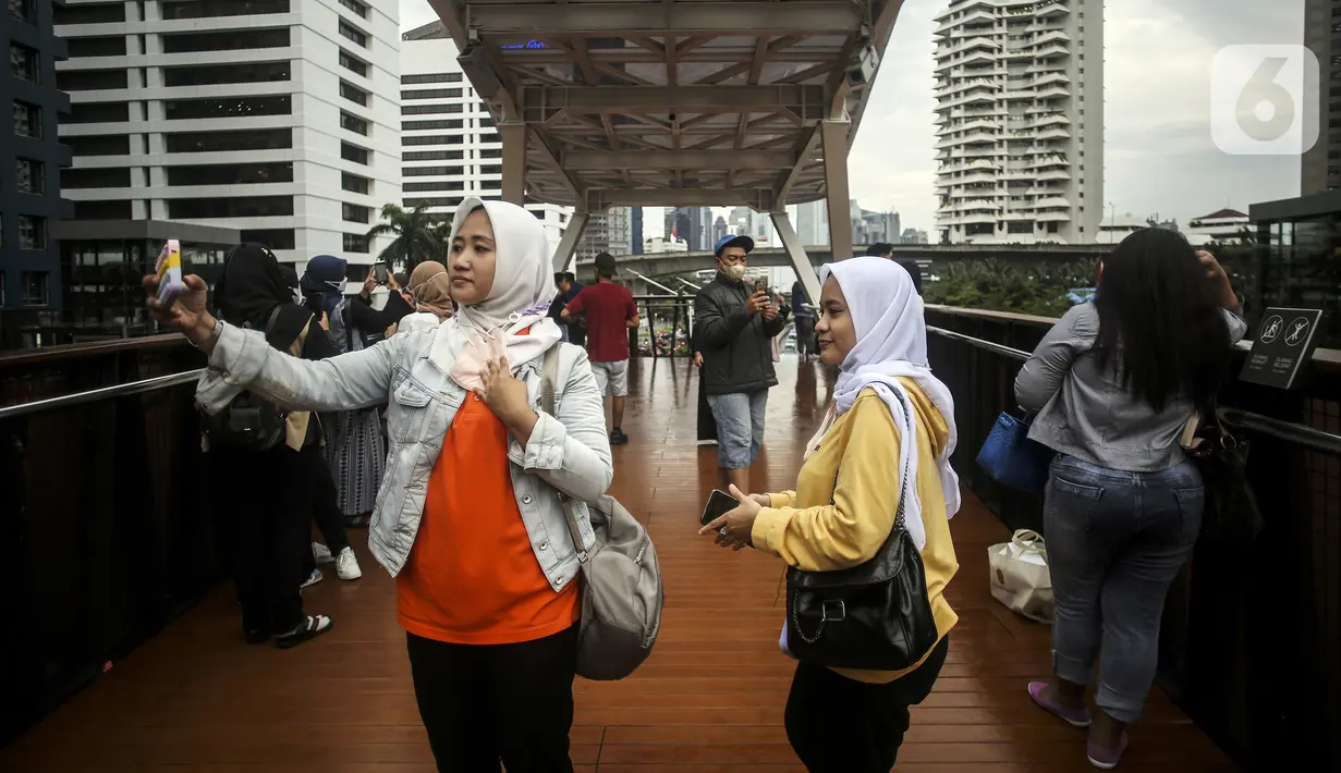 Warga berswafoto dengan kamera ponsel di Jembatan Penyeberangan Orang (JPO) Pinisi, Jalan Jenderal Sudirman, Karet, Jakarta, Selasa (15/3/2022). Belum lama ini, Pemprov DKI Jakarta meresmikan JPO berbentuk spesial tersebut yang membentang di atas Jalan Jenderal Sudirman. (Liputan6.com/Johan Tallo)