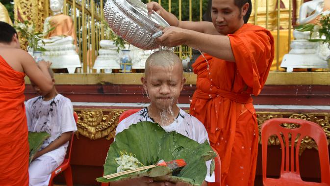 Biksu mengguyur kepala salah satu anak, yang diselamatkan dari gua di Thailand, pada upacara pentahbisan di Kuil Wat Phra That Doi Wao, Chiang Rai, Selasa (24/7). Sebanyak 11 remaja menjalani ritual menjadi biksu. (Panumas Sanguanwong/THAI NEWS PIX/AFP)