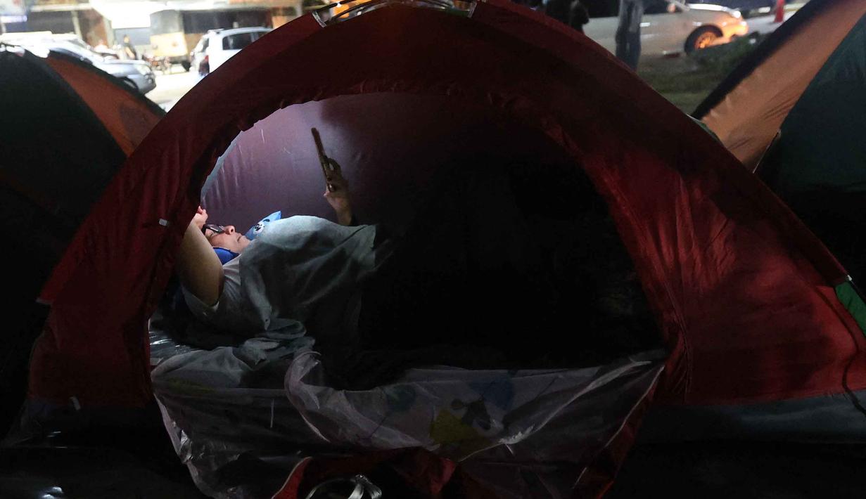 Mereka dengan cemas menanti pembebasan tahanan politik yang telah dijanjikan. Tampak dalam foto, seorang wanita menggunakan telepon seluler di atas tenda yang didirikan oleh kerabat tahanan politik di luar penjara El Rodeo I di Guatire, Negara Bagian Miranda, sekitar 30 kilometer sebelah timur Caracas, Venezuela, pada 12 Januari 2026. (Pedro MATTEY/AFP)