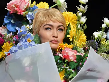 Top model Gigi Hadid mengenakan rancangan rumah mode Moschino saat Milan Fashion Week di Italia, Kamis (21/9). Dalam catwalknya Gigi Hadid mengenakan atribut penuh bunga di tubuhnya. (AFP Photo/Marco Bertorello)