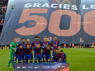 Pemain Barcelona berpose dengan latar belakang spanduk besar penghormatan untuk Lionel Messi yang telah mencetak 500 gol untuk klubnya sebelum pertandingan liga Spanyol antara Barcelona vs Osasuna di stadion Camp Nou, Barcelona (26/4). (AFP/Lluis Gene)