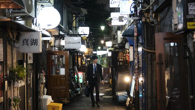 Seorang pria berjalan melalui gang sempit yang dikelilingi bar dan restoran kecil di Golden Gai di distrik Shinjuku, Tokyo (17/7/2019). Gang-gang di kawasan ini merupakan jalan pribadi, bukan jalan umum. (AP Photo / Jae C. Hong)