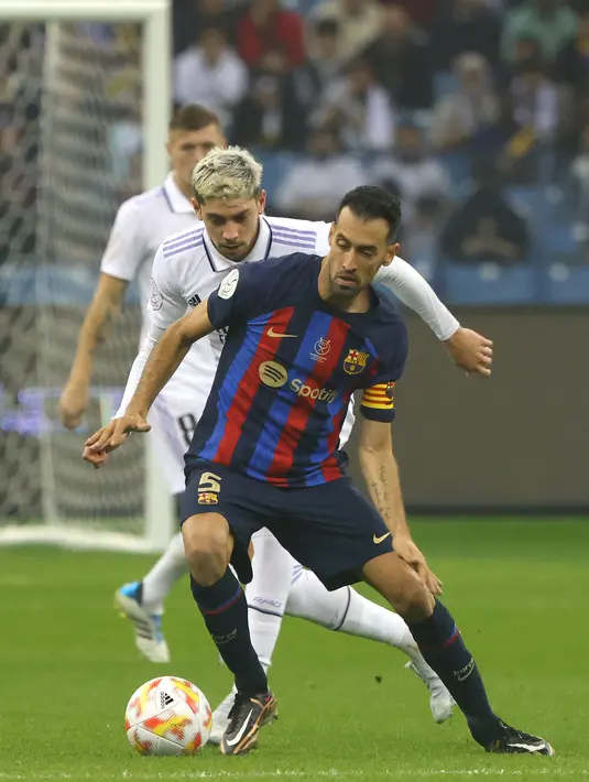 Gelandang Barcelona, Sergio Busquets mengontrol bola dari kawalan gelandang Real Madrid, Federico Valverde selama pertandingan final Piala Super Spanyol di Stadion Internasional Raja Fahd di Riyadh, Arab Saudi, Senin (16/1/2023). Barcelona kini mengoleksi 14 gelar juara sejak Piala Super Spanyol kali pertama digelar pada 1982. (AFP/Fayez Nureldine)