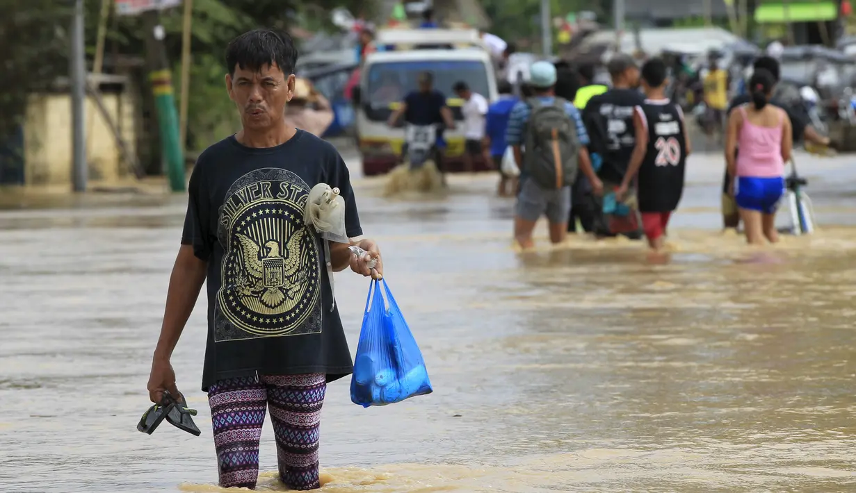 Warga berusaha menyeberangi banjir setelah hujan lebat di Kota Candaba, Filipina (17/12). Ratusan orang mengungsi di atap rumah mereka akibat banjir yang disebabkan topan beberapa hari lalu. (REUTERS/Romeo Ranoco)