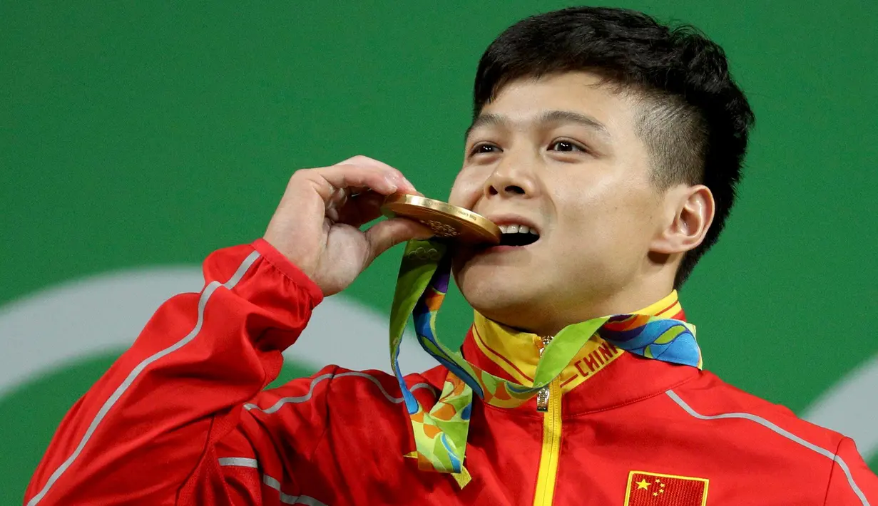 Lifter Tiongkok, Long Qingquan menggigit medali emas yang diraihnya pada Olimpiade Rio 2016 di Rio de Janeiro, Brasil, Minggu (7/8). Long mencetak rekor pada cabang angkat besi kelas 56 kg dengan total angkatan 307 kg. (REUTERS/Stoyan Nenov)