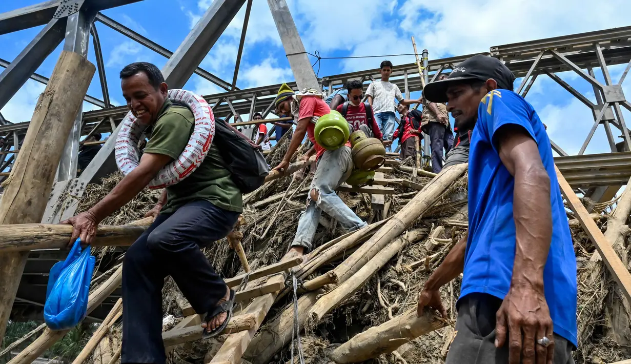 Warga menyeberangi sungai di jembatan yang baru dibangun yang menghubungkan Aceh dan Provinsi Sumatera Utara setelah hancur akibat banjir bandang di Sungai Peusangan, Bireuen, Provinsi Aceh, pada Selasa 9 Desember 2025. Sebagian jembatan rangka baja yang menghubungkan Aceh dan Provinsi Sumatera Utara di Sungai Peusangan, Bireuen, Provinsi Aceh, hancur akibat terjangan banjir bandang pada akhir November 2025 lalu. (CHAIDEER MAHYUDDIN/AFP)