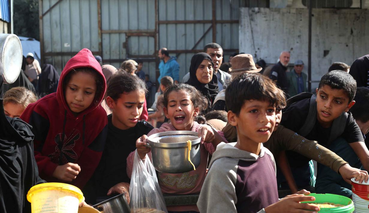 Meski gencatan senjata telah berlangsung sejak 10 Oktober 2025 lalu, pembatasan akses yang diberlakukan, terutama oleh Israel, terus menghambat penyaluran bantuan yang efektif ke wilayah yang sangat membutuhkan. Tampak dalam foto, warga Palestina yang terlantar, anak-anak, dan dewasa, menunggu makanan di sebuah tempat penampungan yang telah dihuni keluarga-keluarga di Nuseirat, pusat Jalur Gaza, pada 23 November 2025. (EYAD BABA/AFP)