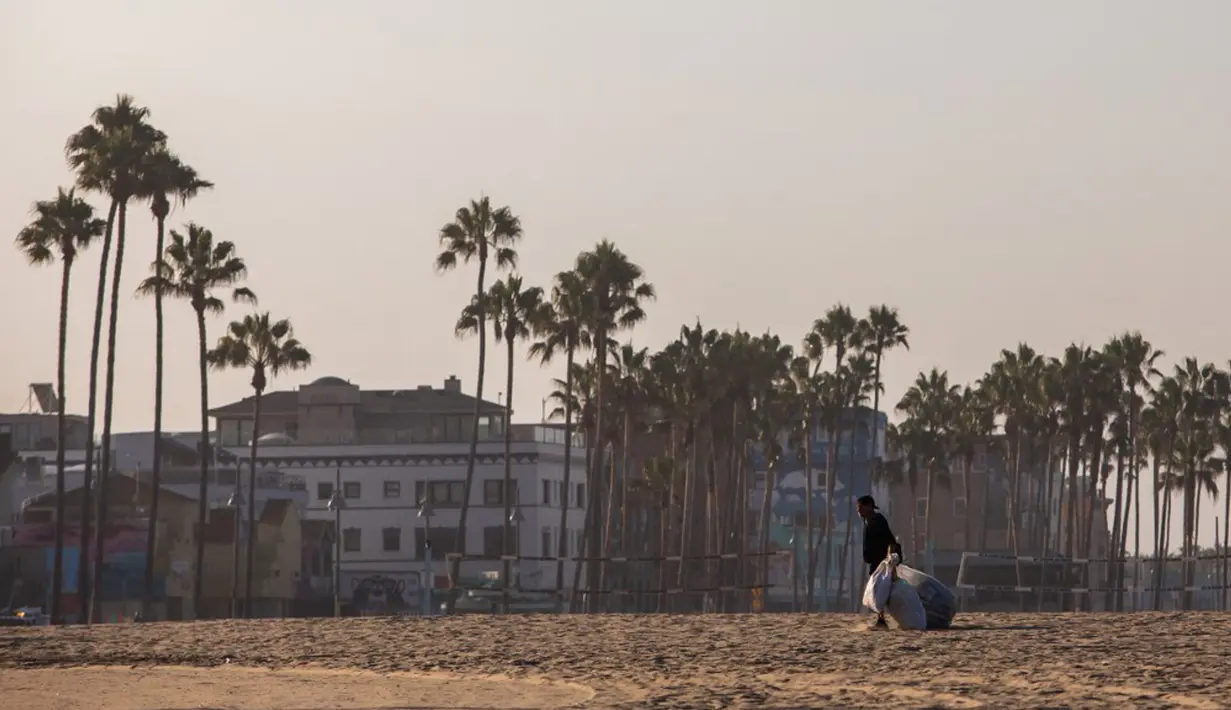 Seorang pria tunawisma berjalan dengan tas bahan daur ulang pada pagi hari di Venesia, California, Amerika Serikat, 12 Agustus 2021. (Apu GOMES/AFP)