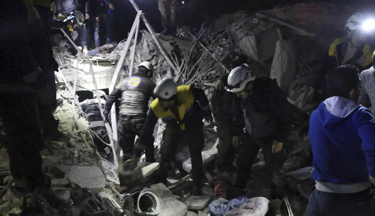 Relawan White Helmets menyingkirkan reruntuhan bangunan untuk mencari korban serangan militer di Provinsi Idlib, Suriah, Minggu, (7/1). Selain menewaskan 25 orang, serangan ini juga melukai 100 lainnya. (Syrian Civil Defense White Helmets via AP)